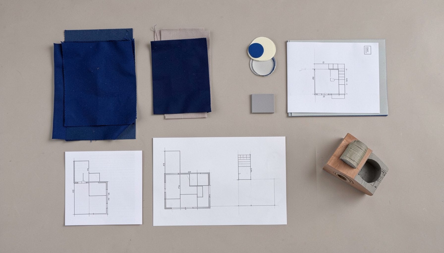 Overhead flat-lay of interior design samples — fabric swatches, paint chips, a floor plan sketch, and a small scale model